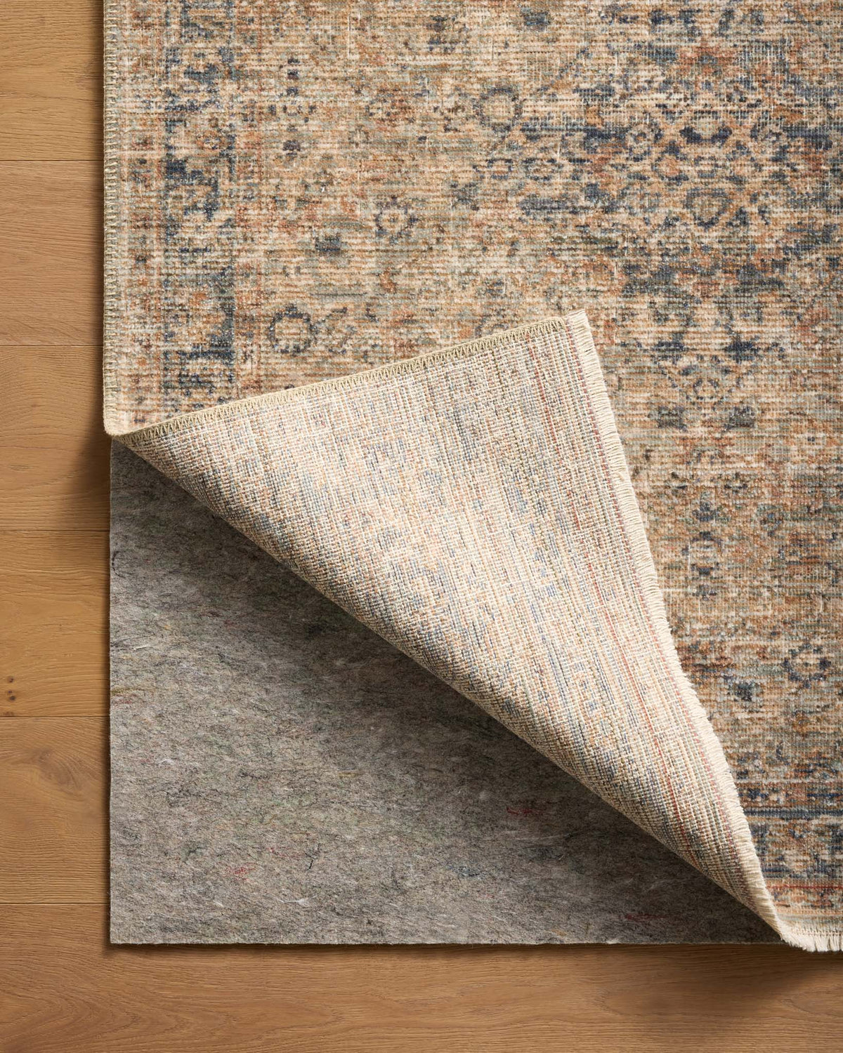 Loloi Loloi- Grip 1/4" Rug Pad in Grey, under a rug, its corner turned back