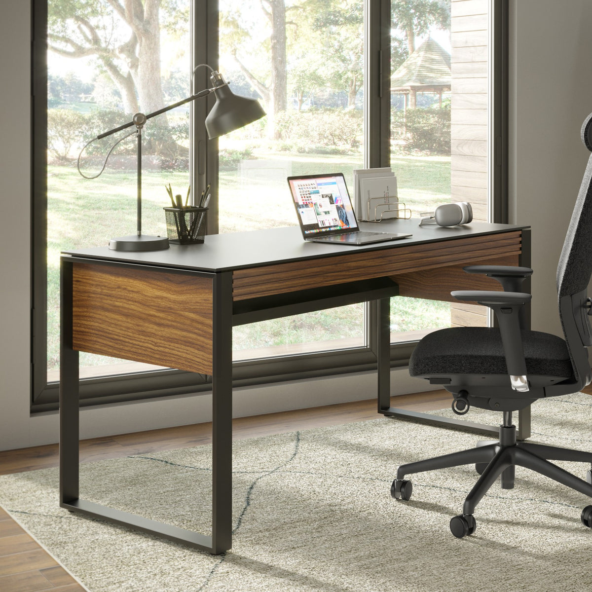 BDi Corridor 6501 Office Desk in Natural Walnut, in a home office by a window, leaning shelves behind