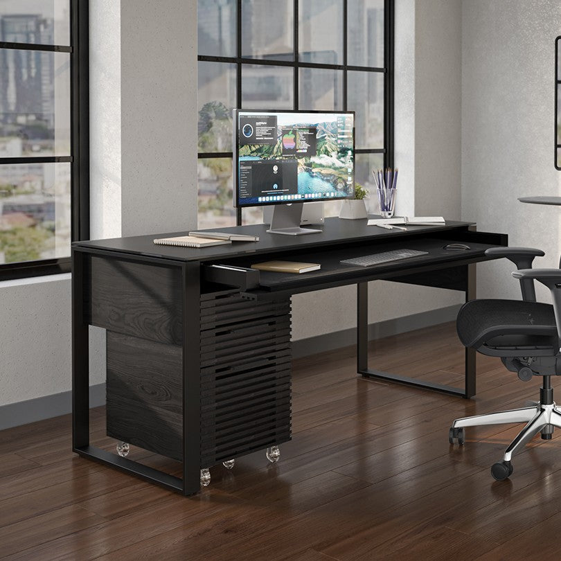 BDi Corridor 6501 Office Desk in Charcoal Stained Ash, with a file pedestal and keyboard tray, in a home office by tall windows