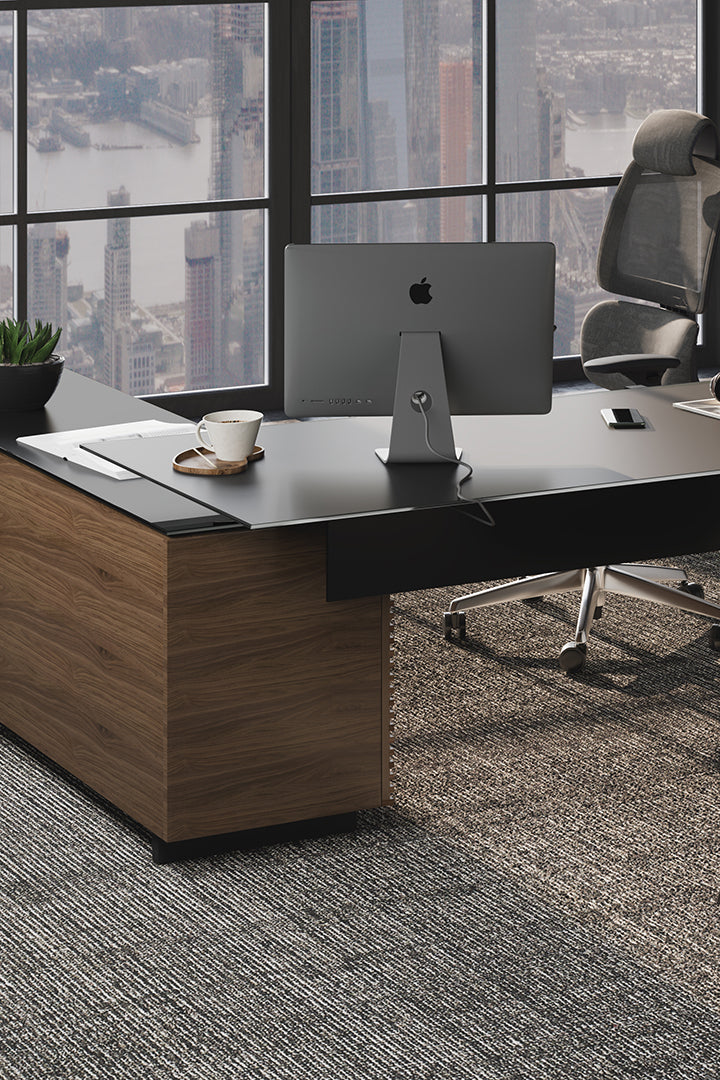 BDi Corridor 6531 L-Shaped Office Desk in Natural Walnut, back corner with a computer, in a high-rise office