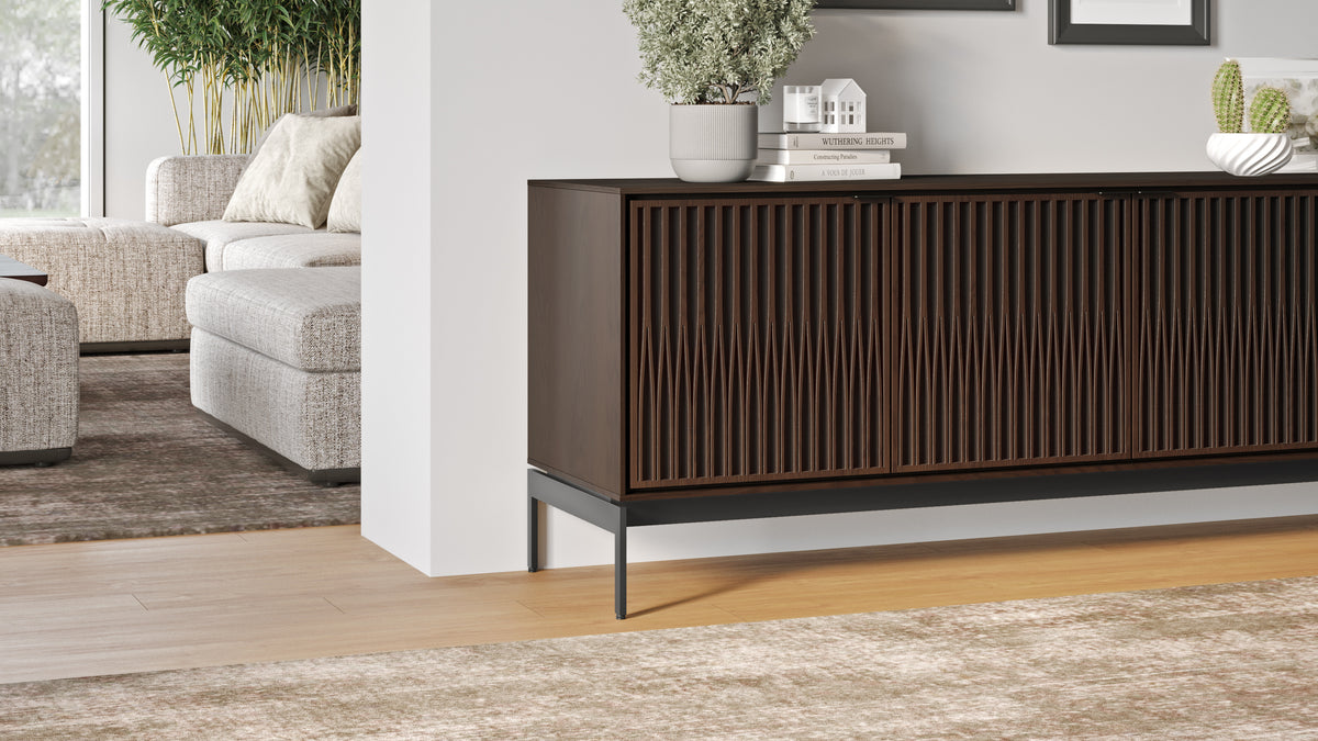 BDi Elements 8709 Media + Storage Console in Toasted Oak, beside a sofa in a living room, with Tune door fronts