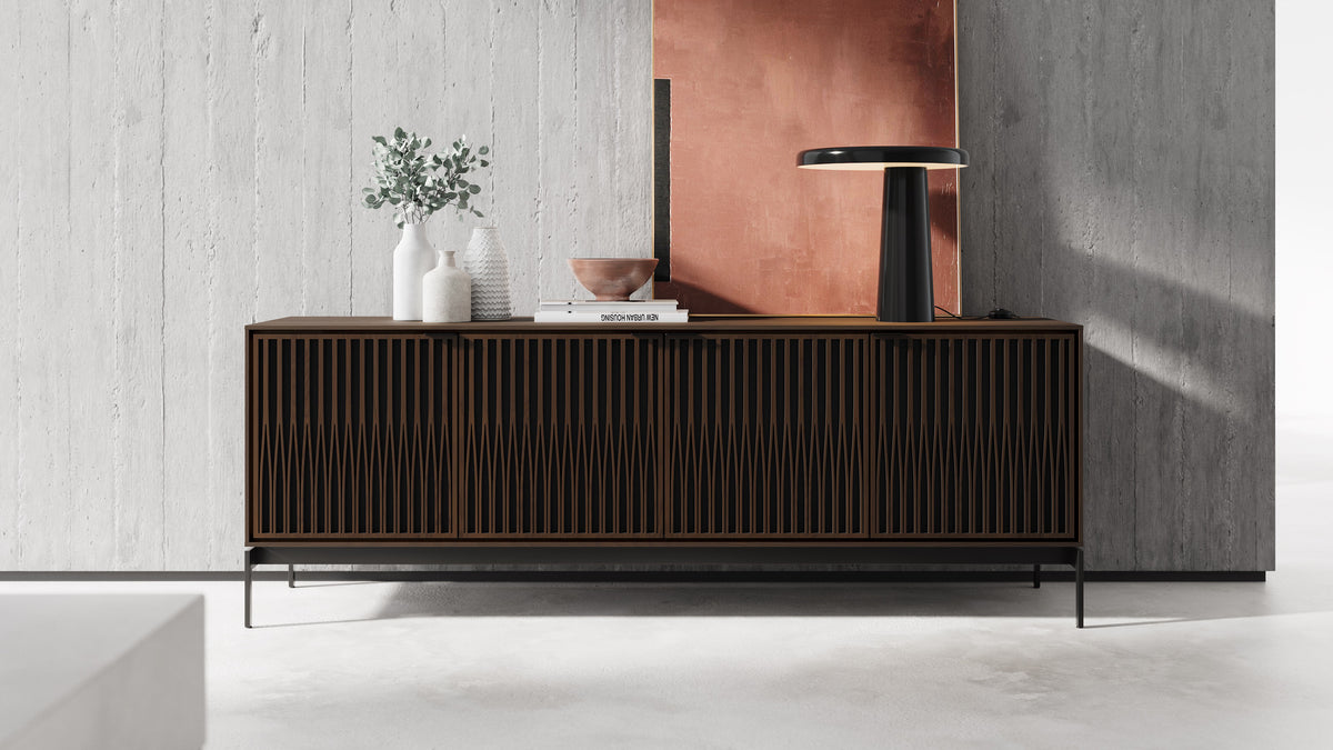 BDi Elements 8709 Media + Storage Console in Toasted Oak, against a concrete wall with a lamp, with Tune door fronts