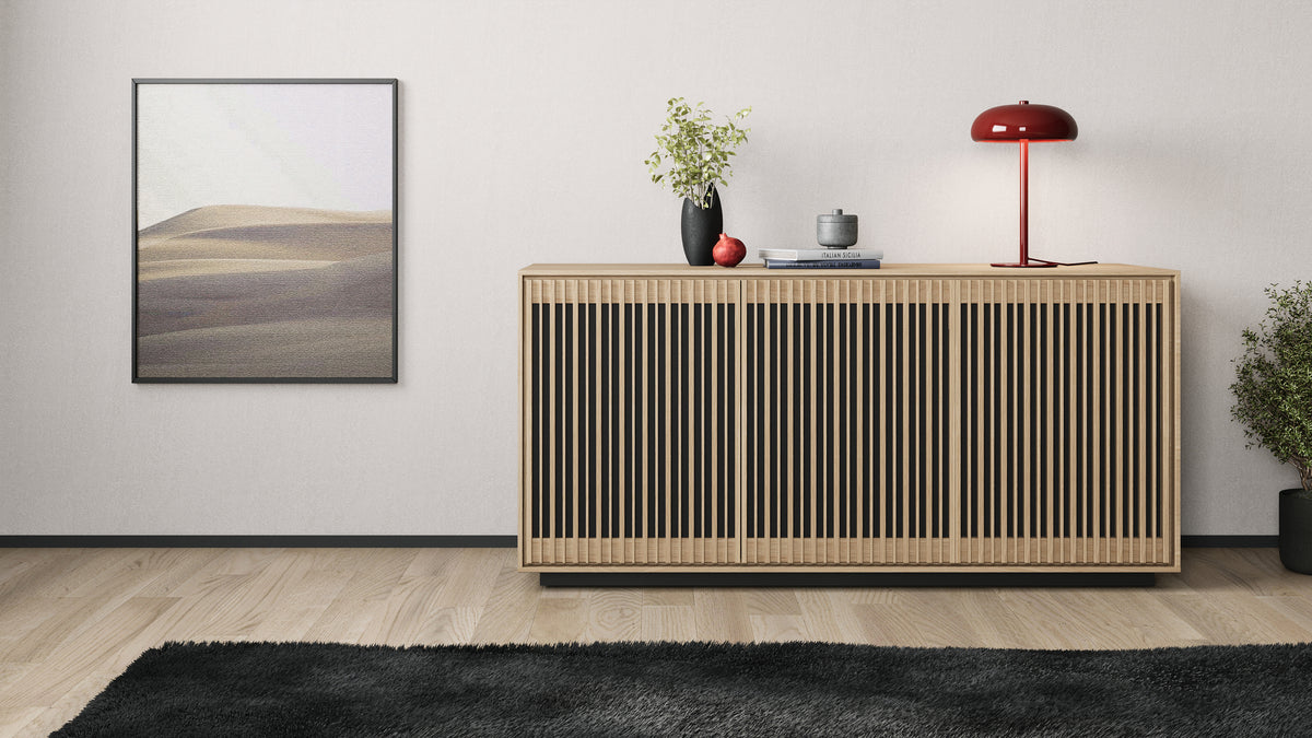 BDi Profile 8477 3-Door Media & Storage Console in Washed Oak, closed, against a wall with a lamp and art