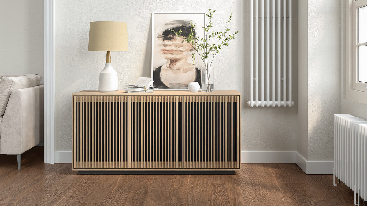 BDi Profile 8477 3-Door Media & Storage Console in Washed Oak, closed, in a living room with a lamp and print
