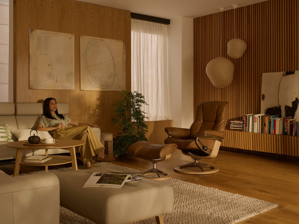 Stressless Mayfair recliner and ottoman in caramel leather beside a cream sofa in a warm living room