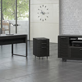 BDi Corridor 6507 Mobile File Cabinet in Charcoal Stained Ash, beside a desk and multi-function cabinet in an office