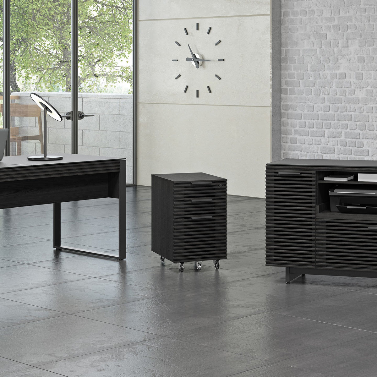 BDi Corridor 6507 Mobile File Cabinet in Charcoal Stained Ash, beside a desk and multi-function cabinet in an office