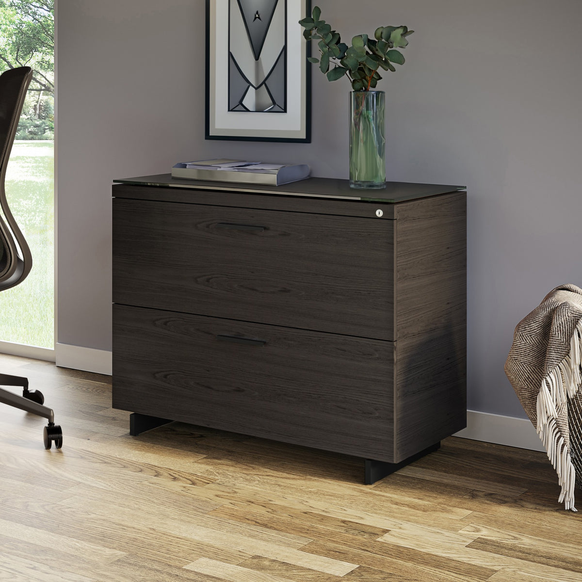 BDi Sequel 20 6116 Lateral File Cabinet in Charcoal Stained Ash, with a black base, beside a desk, in a home office