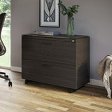 BDi Sequel 20 6116 Lateral File Cabinet in Charcoal Stained Ash, with a black base, beside a desk, in a home office