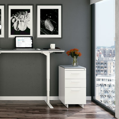 BDi Centro 6414 3 Drawer File Cabinet in Satin White on Oak with Grey Glass, beside a standing desk, in a home office