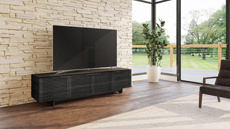 BDi Corridor 8173 Low Profile Media Console in Charcoal Stained Ash, in a room with a stone wall and a TV