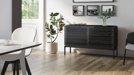 BDi Corridor 7128 Compact 2-Door Storage Cabinet in Charcoal Stained Ash, in a dining room beside a potted plant