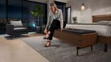 BDi Linq Bench in Pepper | Leather, with a Natural Walnut frame, a woman seated at the foot of a bed