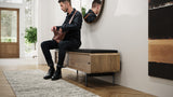 BDi Linq Bench in Pepper | Leather, with a Natural Walnut frame, a man seated in an entryway