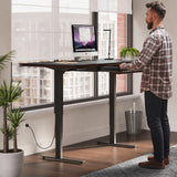 BDi Sequel 20 Sit + Stand Desk in Chocolate Stained Walnut, raised, with a person standing at it, beside a multi-function cabinet