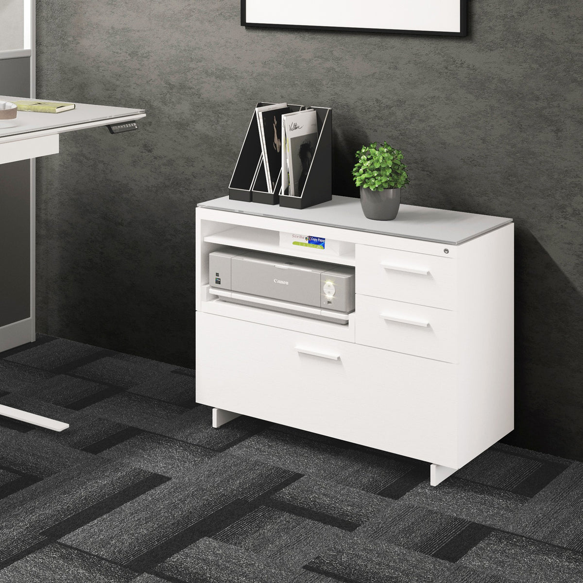 BDi Centro 6417 Multi Function Cabinet in Satin White on Oak with Grey Glass, beside a standing desk, in an office