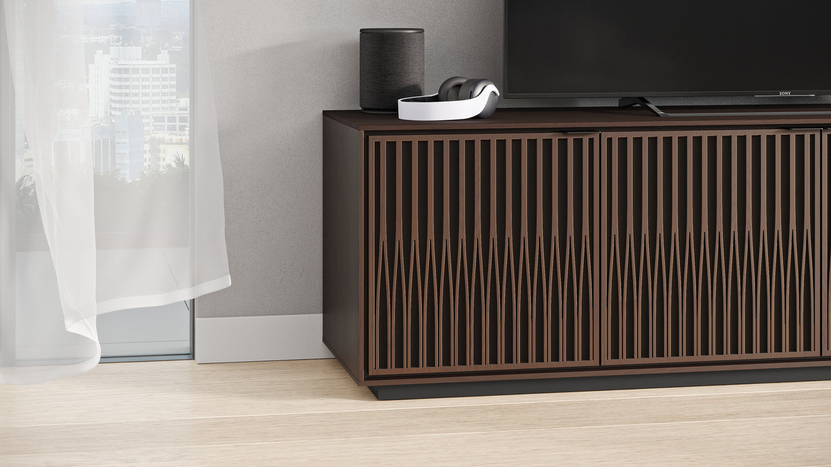 BDi Elements 8703 Media + Storage Cabinet in Toasted Oak, with a TV and a speaker, by a window, with Tune door fronts