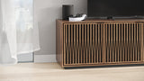 BDi Elements 8703 Media + Storage Cabinet in Natural Walnut, with a TV and a speaker, by a window, with Tune door fronts