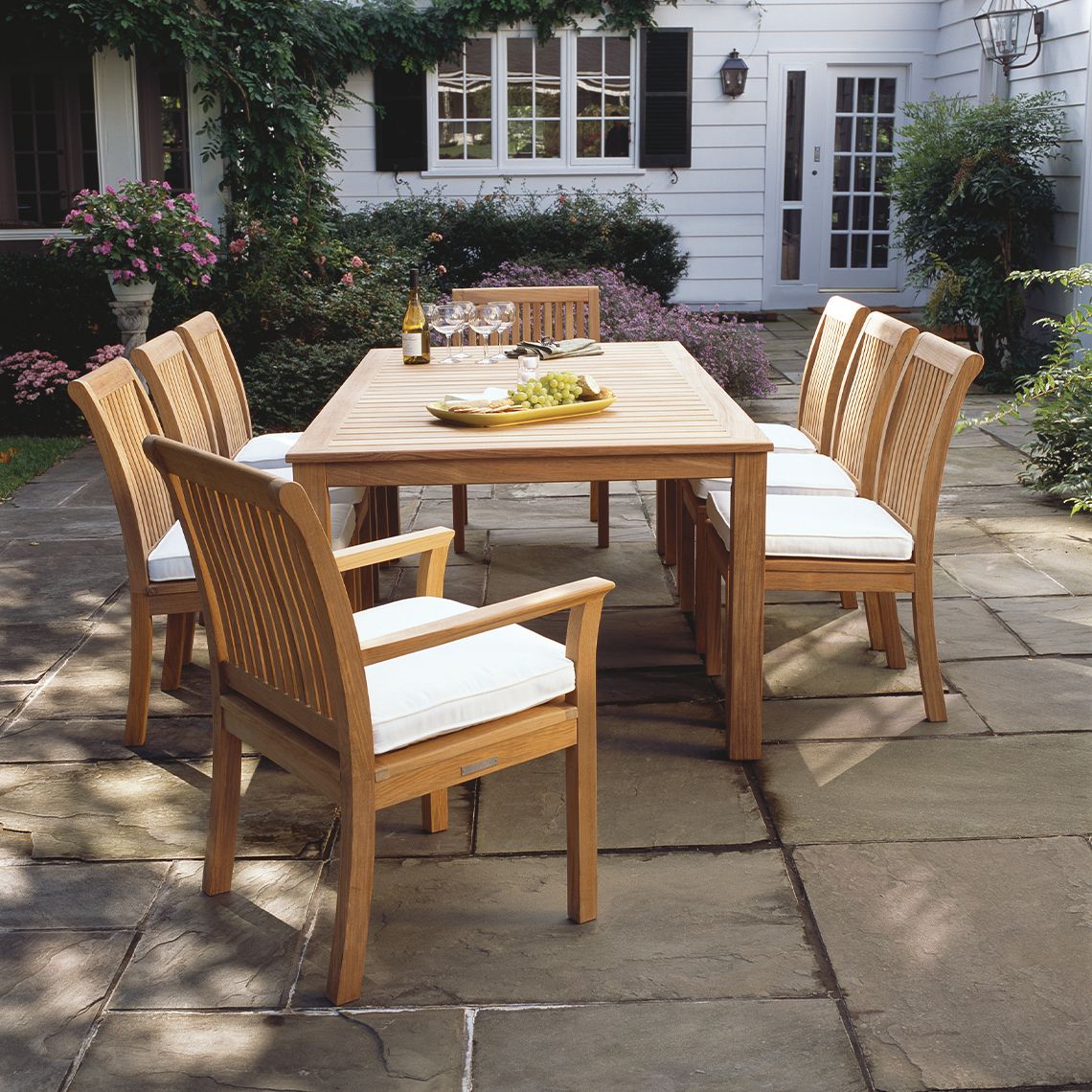 Wooden outdoor dining set with table and chairs on a stone patio.