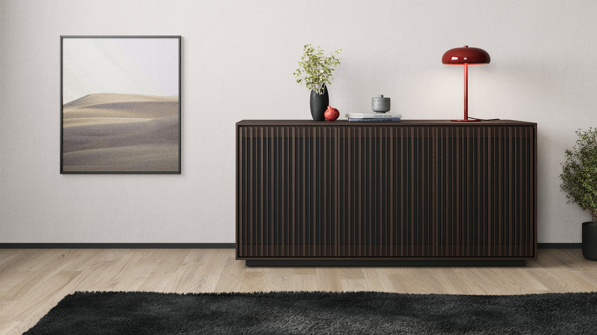 BDi Profile 8477 3-Door Media & Storage Console in Toasted Oak, closed, against a wall with a lamp and art