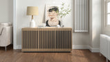 BDi Profile 8477 3-Door Media & Storage Console in Washed Oak, closed, in a living room with a lamp and print