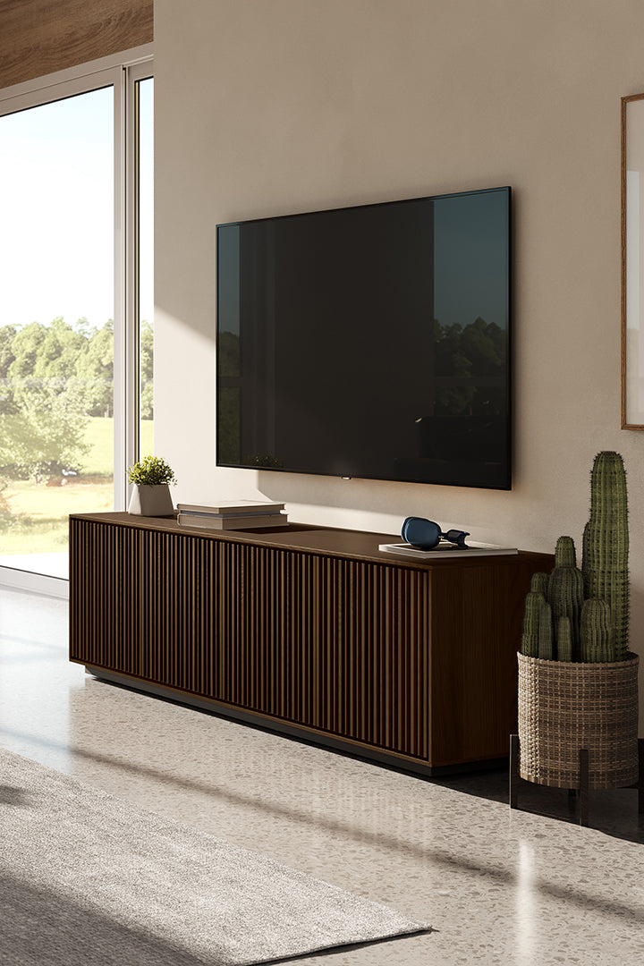BDi Profile 8479 4-Door Media & Storage Console in Toasted Oak, angled, in a living room under a wall-mounted TV