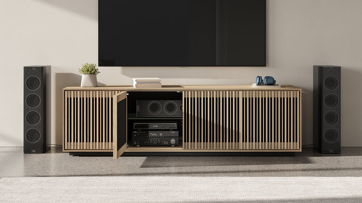 BDi Profile 8479 4-Door Media & Storage Console in Washed Oak, one door open, in a home theatre with tower speakers