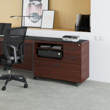 BDi Sequel 20 6117 Multi Function Cabinet in Chocolate Stained Walnut, with a black base, beside a lateral file under a desk top, in an office
