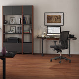 BDi Sequel 20 Sit + Stand Desk in Chocolate Stained Walnut, two desks, one raised, in an office with shelving