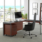 BDi Sequel 20 6107 Mobile File Cabinet in Chocolate Stained Walnut, under an L-shaped desk, in an office with shelving