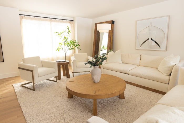 Cream sofa and boucle armchairs around a round wood coffee table in a bright living room